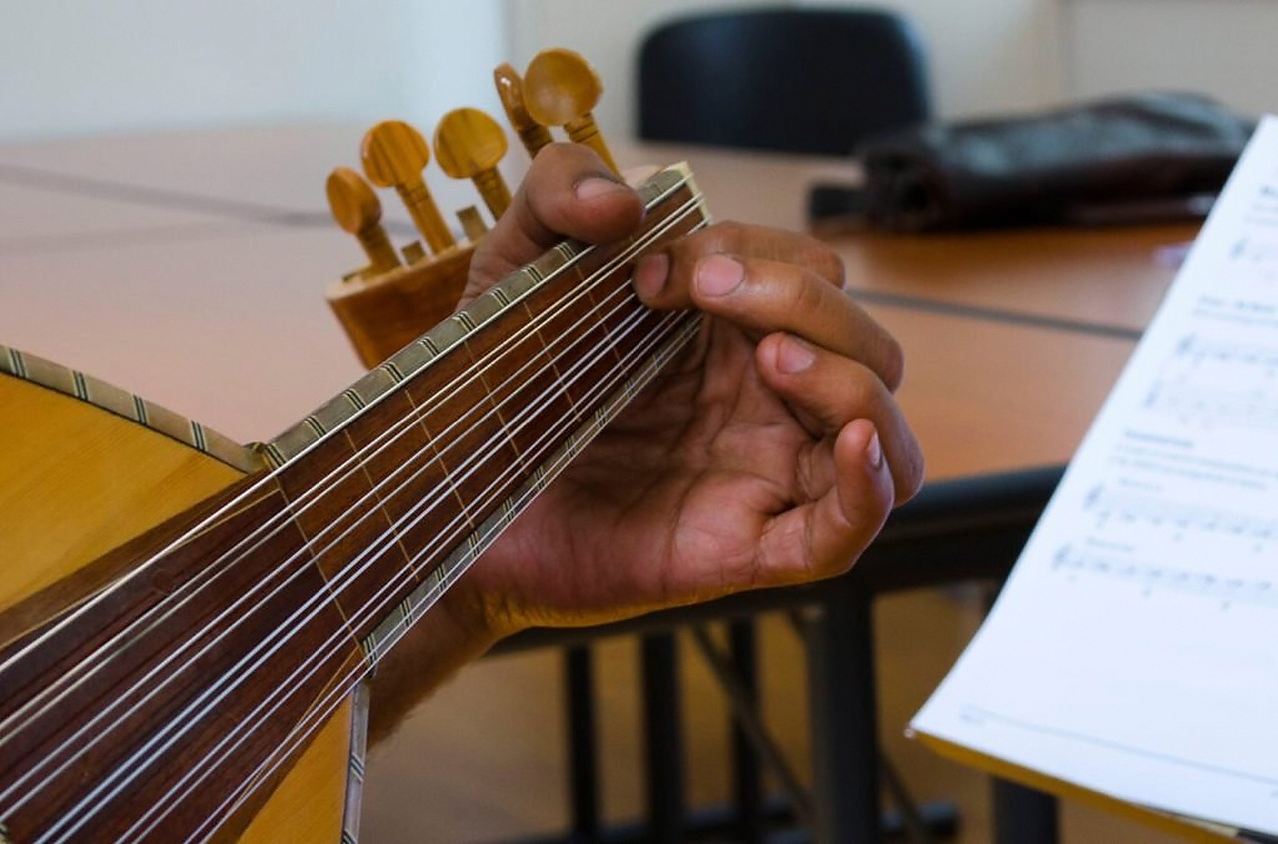 A student's hand fretting the oud during a lesson.