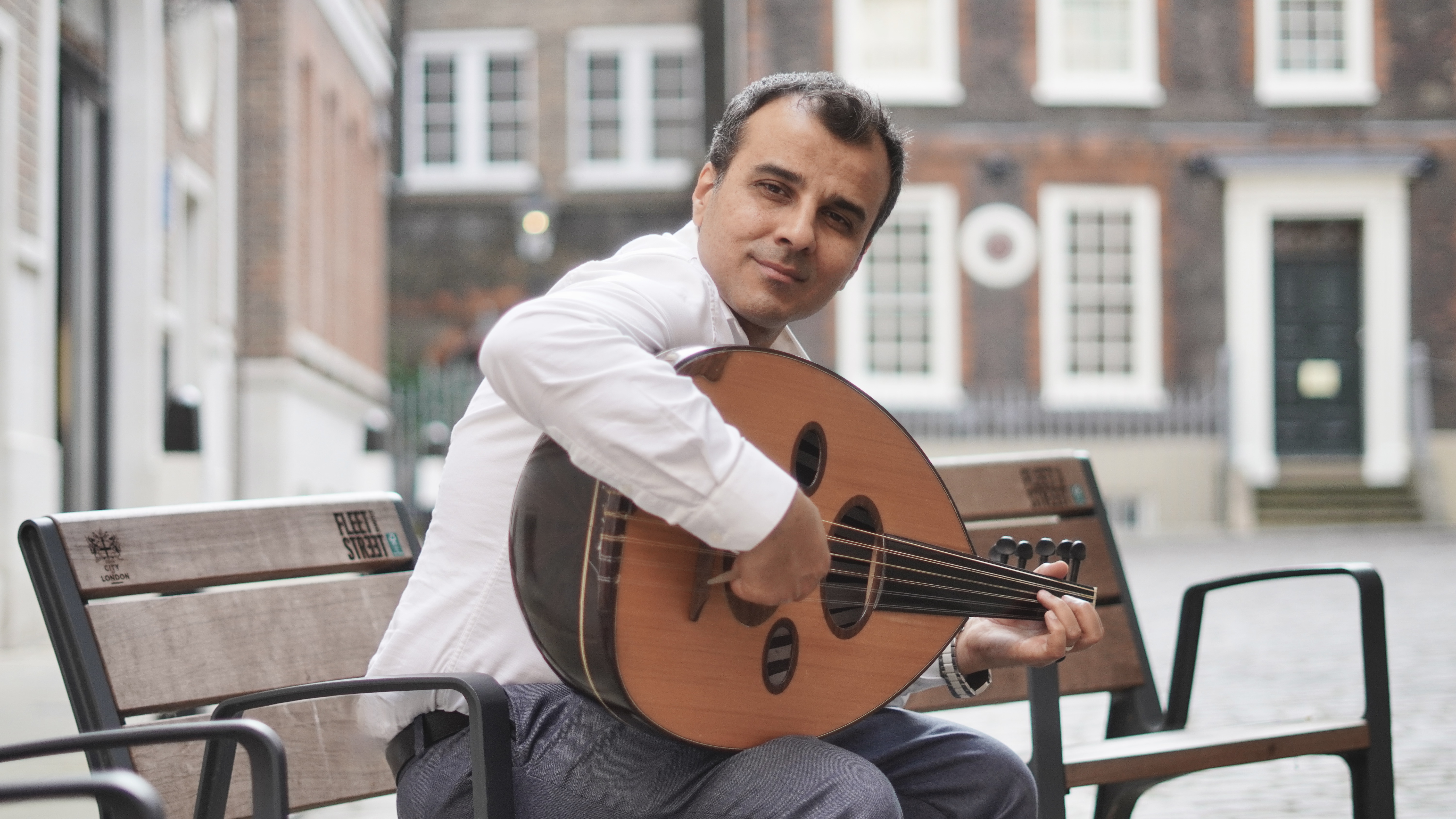 Portrait of Saife Al-Naffakh playing oud at a concert.